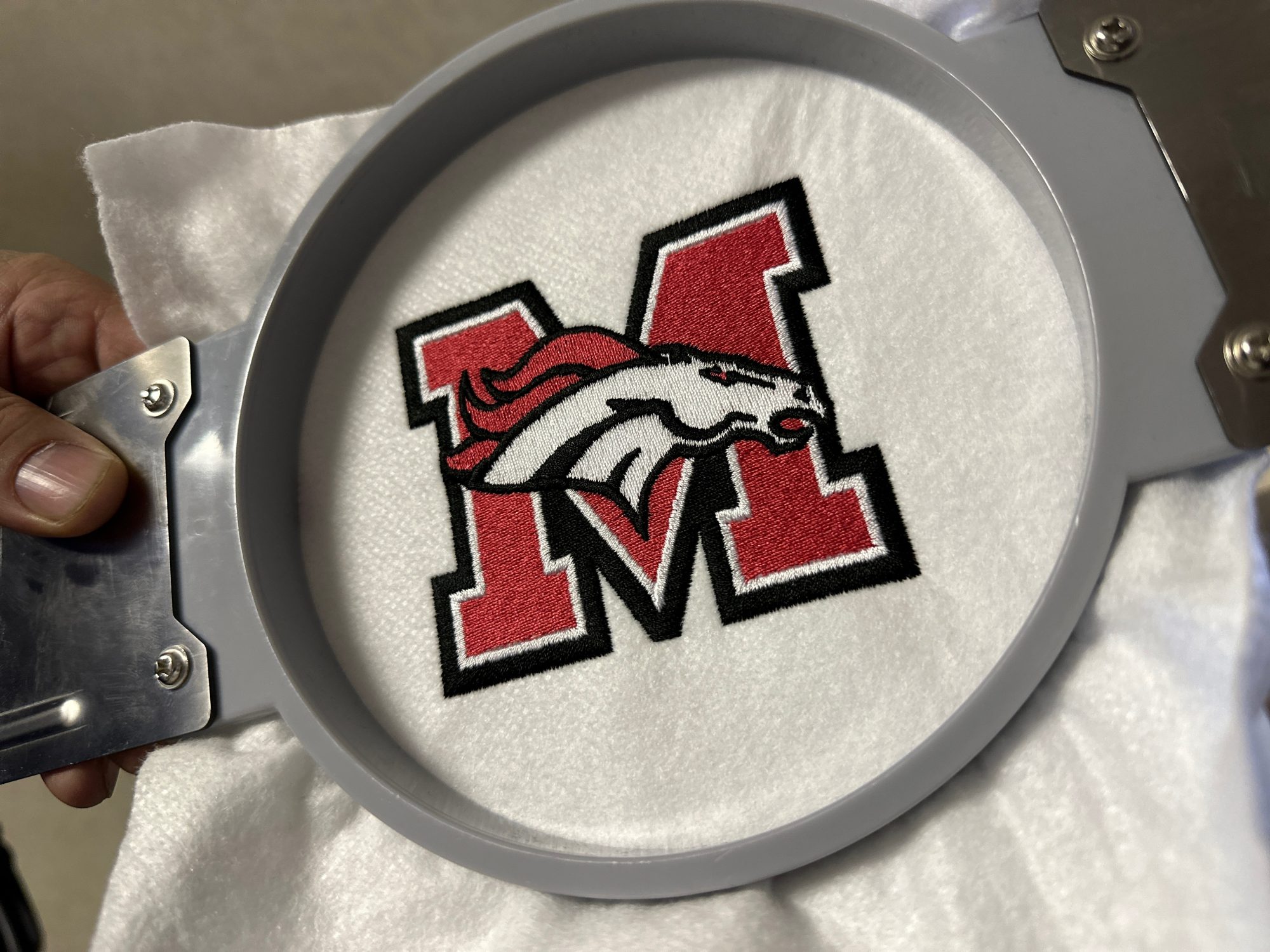 Custom embroidered logo for a local school organization, still on the hoop at The Print Plug embroidery shop